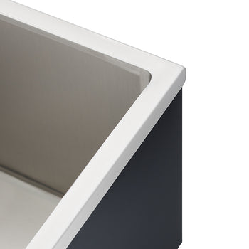 Close-up of the top corner of a rectangular, stainless steel apron-front sink, showcasing the brushed metal interior and the white, sharply defined lip that meets the dark exterior casing. This angle emphasizes the straight lines and contrasting materials of the sink's edge.