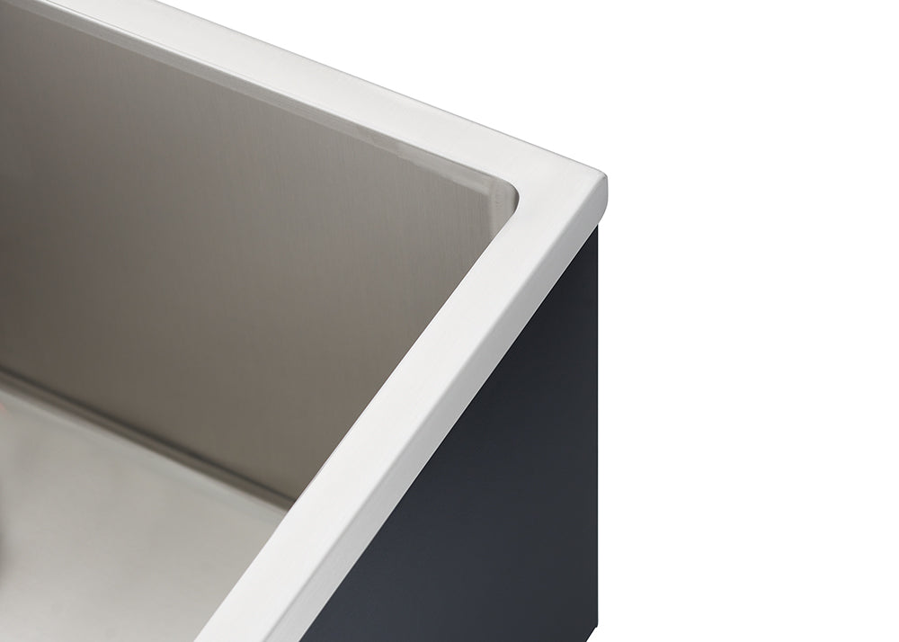 Close-up of the top corner of a rectangular, stainless steel apron-front sink, showcasing the brushed metal interior and the white, sharply defined lip that meets the dark exterior casing. This angle emphasizes the straight lines and contrasting materials of the sink's edge.
