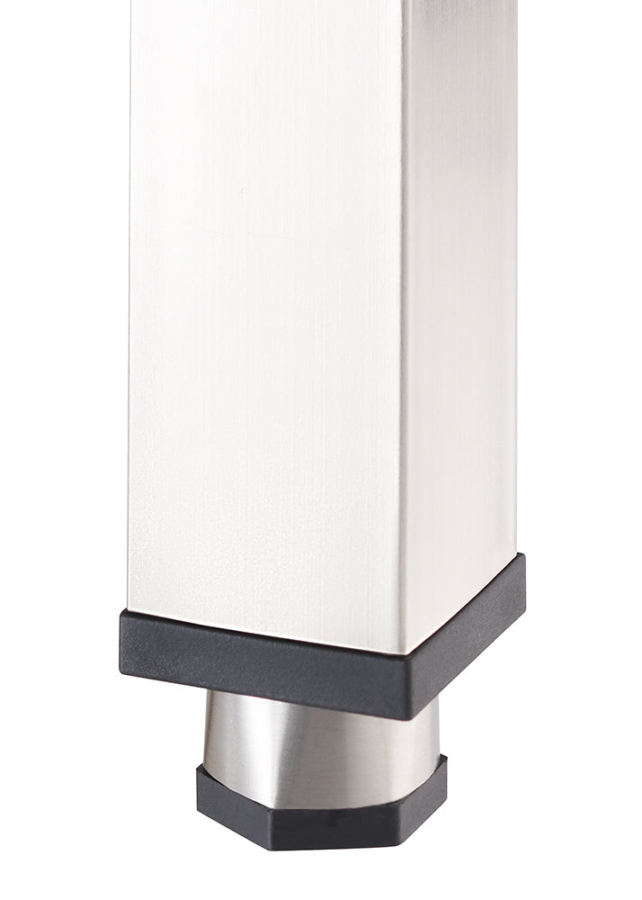 A close-up photograph focuses on the bottom end of a square, brushed metal furniture leg, likely stainless steel. The leg is capped with a black plastic foot or glider that transitions to a smaller, angled metal cylinder at the very base, which is also capped with black plastic.