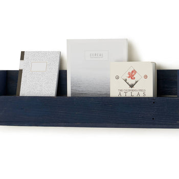 A dark blue wooden shelf is mounted on a white wall, holding three books including 