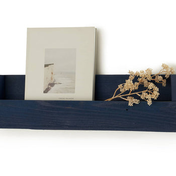 A navy blue wooden shelf is mounted on a white wall, holding a book titled 