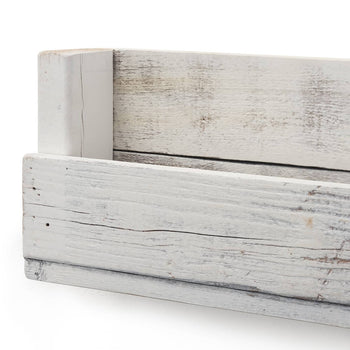 A close-up shot shows the corner of a rustic, whitewashed wooden shelf. The shelf is made of reclaimed wood with visible grain and texture, giving it a weathered, vintage appearance.