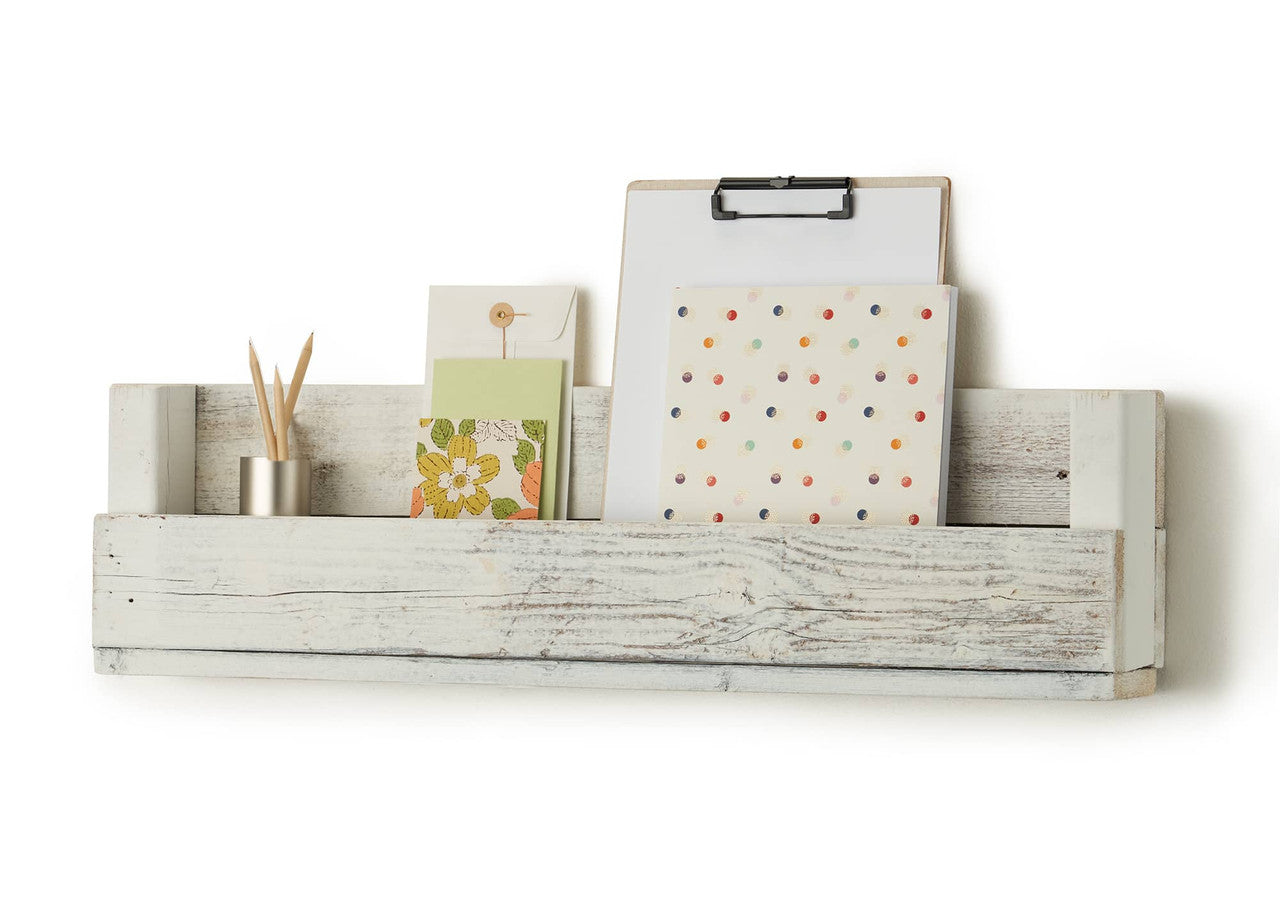 A white wooden shelf, made from reclaimed wood, is mounted on a white wall. The shelf has a rustic, weathered appearance and is holding a clipboard, a notebook, a greeting card, an envelope, and a small metal container with pencils.