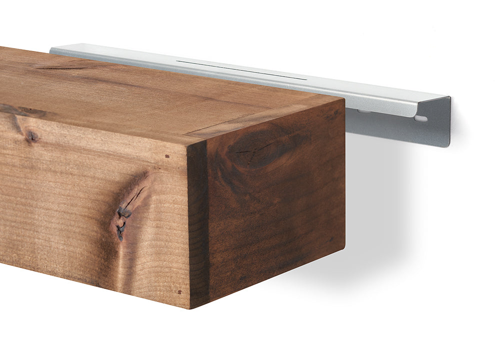 A solid, rustic wooden floating shelf is shown next to a sleek silver metal wall bracket. The wood features a natural grain and knots, while the bracket is designed to be hidden behind the shelf once installed.