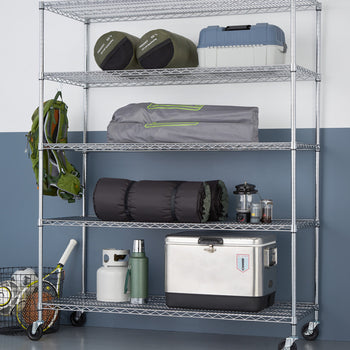 A five-tier wire shelving unit on wheels holds various camping and sports equipment against a two-toned wall. The shelves contain items like sleeping bags, a tent, a cooler, and sports balls, showcasing organized storage.