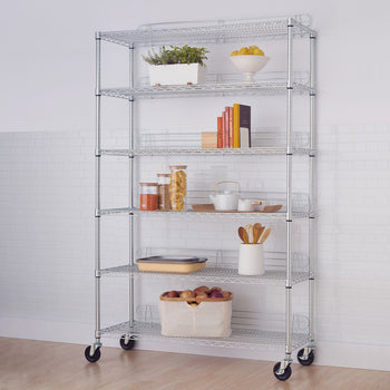 A tall, chrome wire shelving unit with six tiers is filled with various household items. The shelves hold plants, books, kitchenware, and food items, with the unit itself having wheels for mobility.