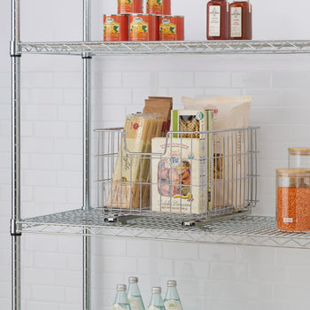 A sliding chrome wire basket filled with various pasta packages and boxes sits on a metal wire shelf. The basket appears to be a sliding drawer, with runners visible at its base, on a shelving unit.