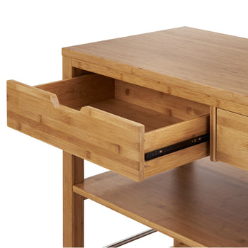 An open drawer of a light wood kitchen island or desk is shown, revealing the interior of the drawer and the metal glides. The furniture piece is made of bamboo or a similar light-colored wood, with visible horizontal grain patterns.
