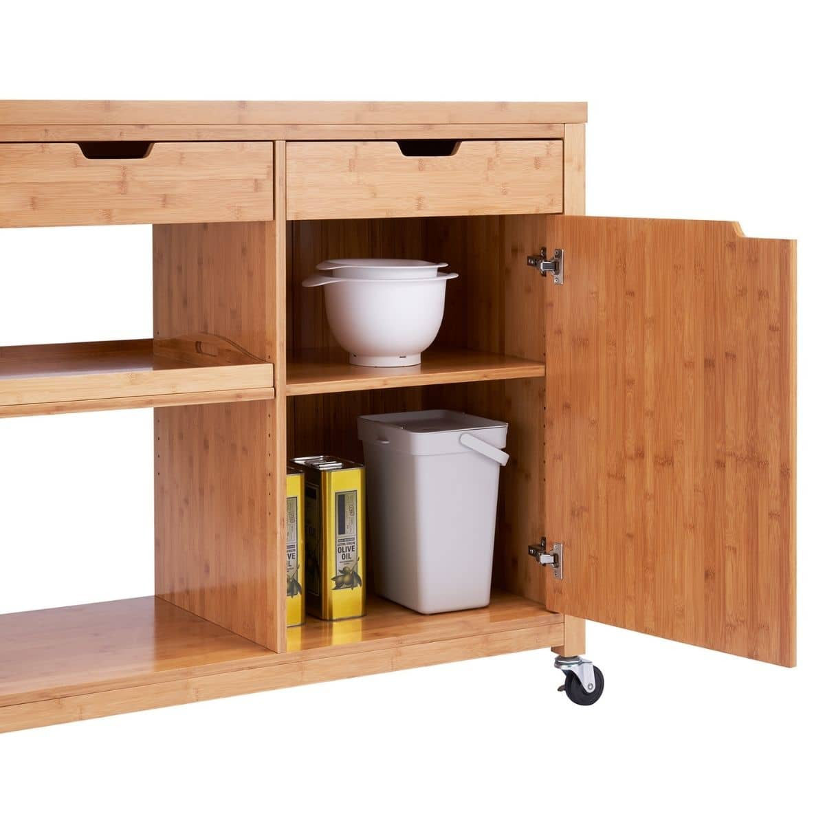 A close-up shot shows a light brown bamboo kitchen island on wheels with drawers, shelves, and a cabinet with its door slightly ajar. Inside the cabinet, there is a white mixing bowl with a lid on the top shelf, and a light gray waste bin and two yellow olive oil tins on the bottom shelf.