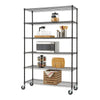 A six-tier Trinity Basics wire shelving unit in black, equipped with wheels, holds various kitchen and pantry items. The shelves display a microwave, spice rack, cutting boards, glassware, a jar of oats, and a wooden crate with a towel.