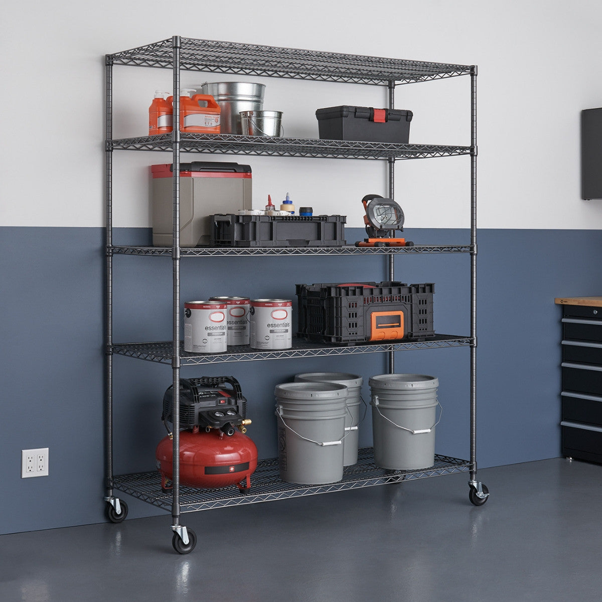 A five-tier black wire shelving unit stands against a two-toned wall, holding various storage containers, buckets, and tools. The shelving unit has wheels and is placed on a gray floor.