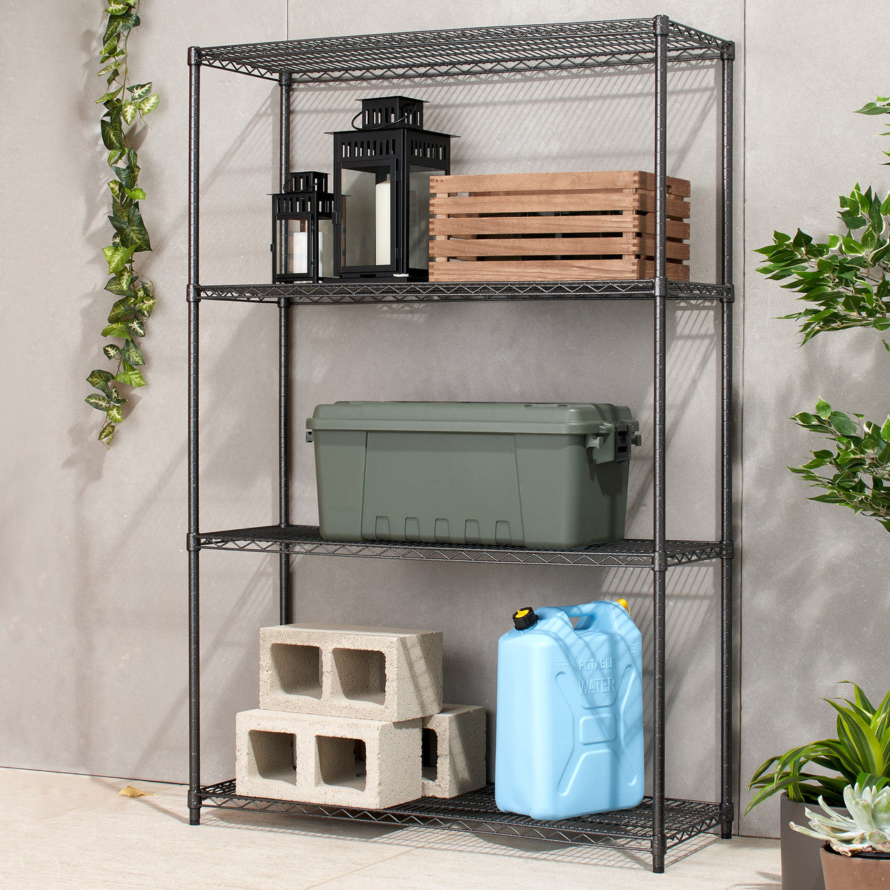 A four-tier black wire shelving unit stands against a light gray tiled wall. The shelves hold various items including lanterns, a wooden crate, a green storage bin, concrete blocks, and a blue water jug.