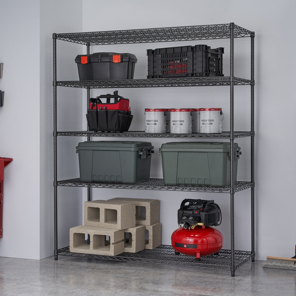 A black anthracite wire shelving used in a garage filled with tote boxes, paint cans, cinder blocks, air compressor, and other home garage items.