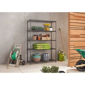 A five-tier black wire shelving unit stands against a light gray wall, holding various gardening supplies such as potted plants, bags of soil, and gardening tools. To the left of the shelving unit is a beige hose reel with a green hose.