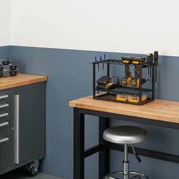 A workbench in a garage or workshop with a black metal organizer rack holding two cordless drills, batteries, and other tools. On the left, another workbench with drawers has several small parts storage boxes.