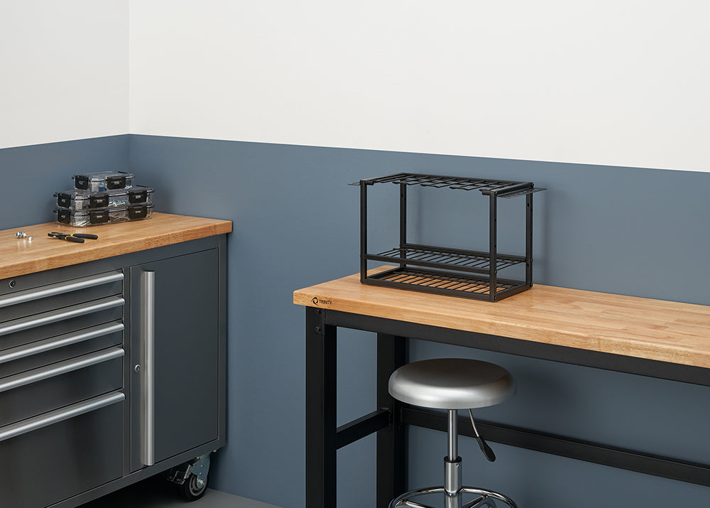 A workbench with a butcher-block top stands in a workshop, featuring a metal tool organizer and a silver stool. On the left, a rolling metal cabinet with several clear plastic storage boxes rests on a matching countertop.