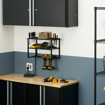 A well-organized garage workbench features a two-tone wall, with a light gray top half and a dark blue bottom half. A black metal shelf with hanging hooks holds two yellow and black cordless drills, two spare batteries, a charger, and various small hand tools.
