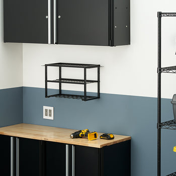 A neatly organized workshop or garage with a workbench and black cabinets against a two-toned wall. On the workbench, a drill and batteries are visible, while a black wire rack shelf is mounted on the wall above it.