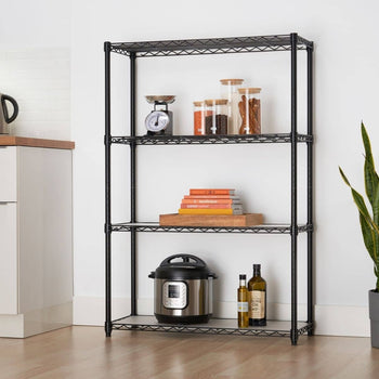 A black four-tier wire shelving unit stands against a white wall, holding various kitchen and household items. The shelving appears sturdy and functional, providing open storage in a room with a light wood floor.