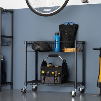 A black metal wire shelving cart with wheels holds various items, including a toolbox, water bottle, backpack, and helmet, against a blue wall. A taller, similar shelving unit is partially visible on the left, and a bicycle wheel hangs above.