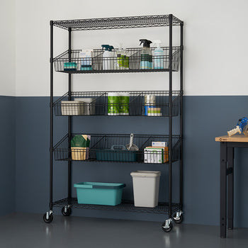 A black, five-tier wire shelving unit on wheels stands against a two-tone blue and white wall, holding various storage bins and items. A wooden table with a stool and packing supplies is visible to the right.