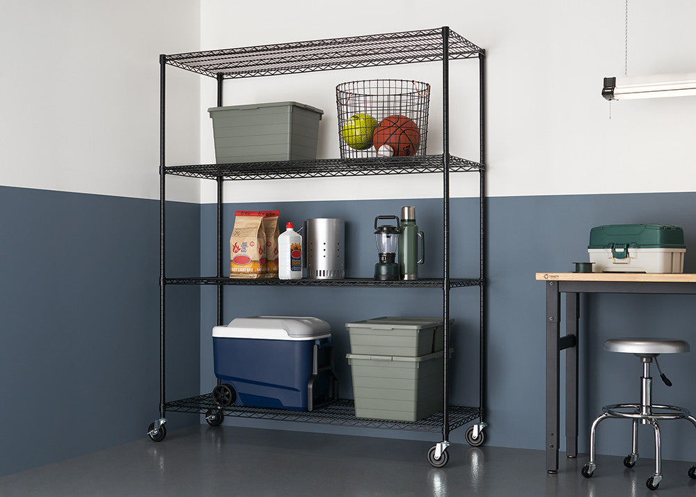 A black wire shelving unit with three tiers is shown in a garage setting, holding various items like bins, a basketball, and a cooler. The shelving unit has wheels and is positioned against a two-tone wall, with a workbench and stool visible in the background.