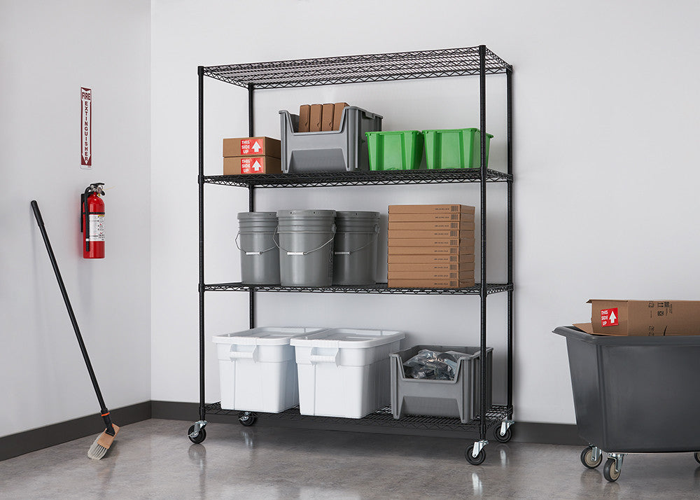 A black wire shelving unit with four tiers is filled with storage bins and boxes in a clean, industrial setting. The unit is on wheels and sits against a white wall, next to a red fire extinguisher and a broom.