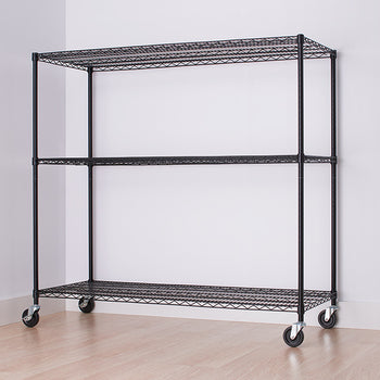 A black wire shelving unit with three tiers and wheels is centered against a white wall. The unit is empty, and a partial view of a white cabinet with drawers is visible on the right side of the image.