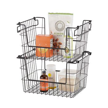A set of two black wire stacking baskets filled with pantry items, including almond flour, baking soda, a bottle of oil, and a container of sugar. The baskets have handles that allow them to be stacked or used separately for storage organization.
