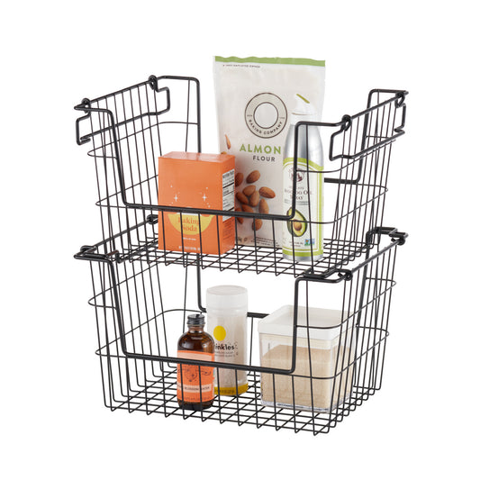 A set of two black wire stacking baskets filled with pantry items, including almond flour, baking soda, a bottle of oil, and a container of sugar. The baskets have handles that allow them to be stacked or used separately for storage organization.
