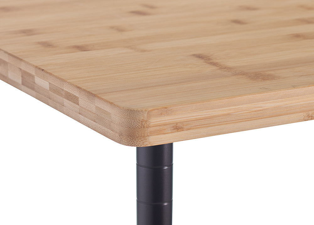 A close-up image of a wooden tabletop with rounded edges, supported by a black metal leg. The tabletop appears to be made of laminated bamboo with a smooth, polished finish.