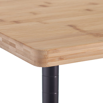 A close-up image of a wooden tabletop with rounded edges, supported by a black metal leg. The tabletop appears to be made of laminated bamboo with a smooth, polished finish.