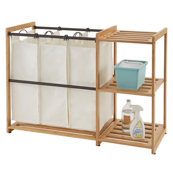 A Bamboo Laundry Station features a light brown bamboo frame with three cream-colored laundry bags suspended from a metal rod. To the right, integrated bamboo shelves hold a teal basket and two bottles of cleaning products.