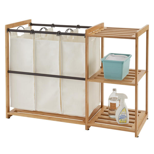 A Bamboo Laundry Station features a light brown bamboo frame with three cream-colored laundry bags suspended from a metal rod. To the right, integrated bamboo shelves hold a teal basket and two bottles of cleaning products.