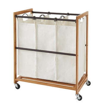 A Laundry Cart with a wooden frame and three removable, natural-colored canvas bags hanging from a metal rod. The cart is on wheels, and there's an additional bronze horizontal metal bars across the frame for stability.