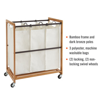 A Trinity 3-Bag Bamboo Laundry Cart features a light brown bamboo frame with dark bronze poles holding three cream-colored, machine-washable polyester bags. The cart is on four swivel wheels, two of which are locking.