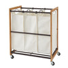 A bamboo laundry cart with 3 white cotton bags and bronze metal bottom shelf.  The sorter is on wheels, allowing for easy portability. 