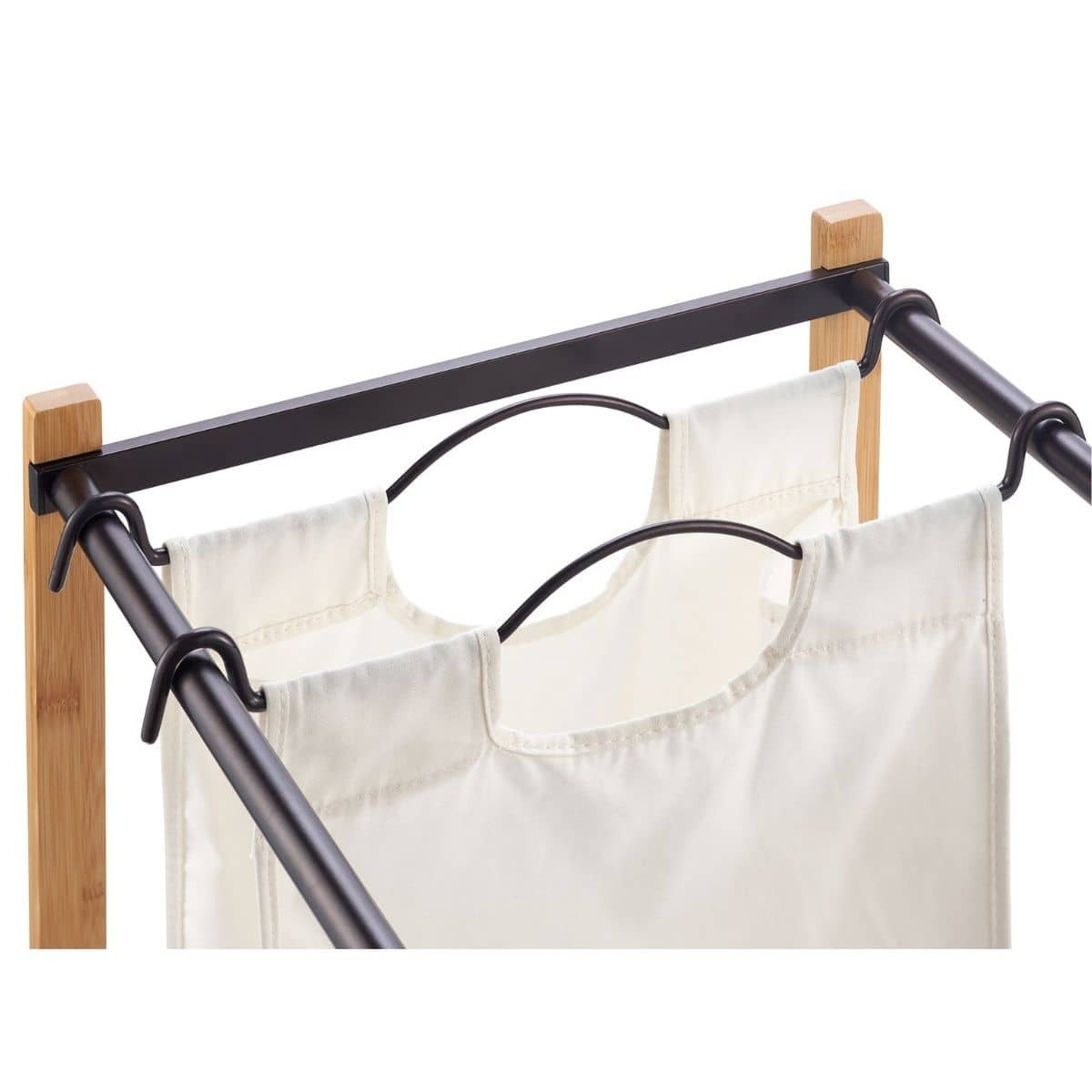 A close-up shows a double laundry hamper with two off-white canvas bags hanging from black metal frames and hooks attached to light brown wooden supports. The focus is on the top portion of the hamper, highlighting the construction and materials.