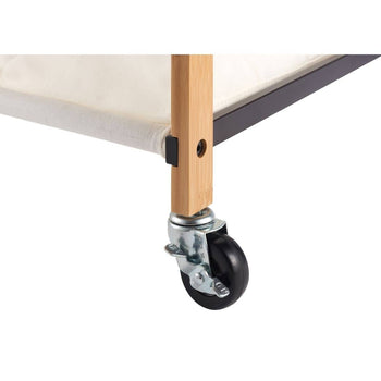 A close-up shot shows the bottom corner of a laundry cart. A light-colored bamboo leg connects to a black metal frame, and a black caster wheel with a silver swivel mount is attached to the bottom of the leg.