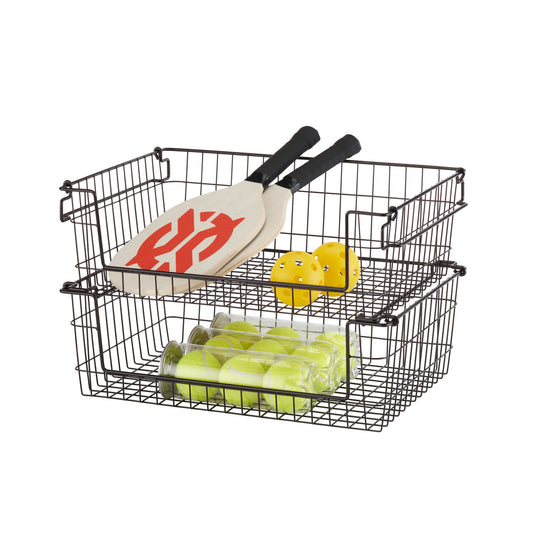 A close-up shot of two dark bronze wire baskets stacked on top of each other, filled with tennis balls, paddles, and yellow stress balls. The baskets are square-shaped with a grid-like wire construction and small handles on the sides.
