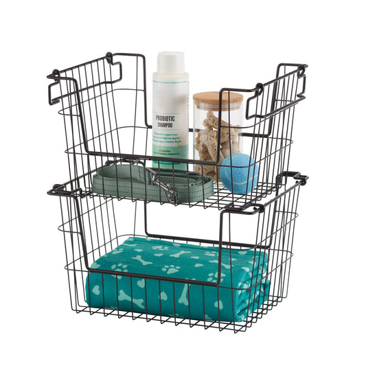A black wire storage basket with two tiers holds various pet care items. The top tier contains a bottle of probiotic shampoo, a jar of dog treats, a blue tennis ball, and a green leash, while the bottom tier holds a folded teal pet blanket with a bone and paw print pattern.