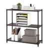 A 3-tier dark bronze metal shelving unit is shown holding various office supplies. The top shelf features a small plant, a calendar displaying June 15, and a white organizer with pens and mail, while the middle shelf holds a multi-slot paper organizer. The bottom shelf contains two white magazine files filled with notebooks and two rectangular storage boxes.