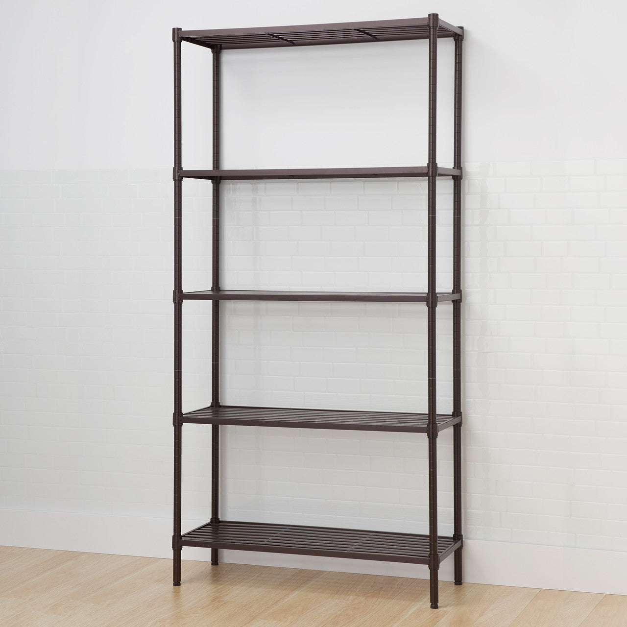 A tall, five-tier dark bronze metal shelving unit stands against a white subway tile wall and light wood floor. The shelves are slatted, and the unit appears sturdy and designed for storage.