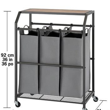 A laundry cart with three gray fabric bags hanging from a metal frame with a wooden top. The cart has wheels and measurements are shown in centimeters and inches.