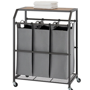 A laundry cart with three gray fabric bins hanging beneath a wooden top, all encased in a dark metal frame with wheels. A folded white towel rests on the wooden surface.