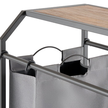 A close-up shot of a laundry cart with three gray fabric bags hanging from metal rods. The cart features a wooden top and a dark metal frame.