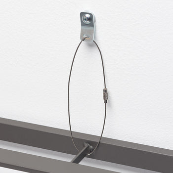 A close-up shot shows a metal picture hanging hook attached to a white wall with a screw. A thin, dark wire loop extends from the hook, connecting to a metal frame below.