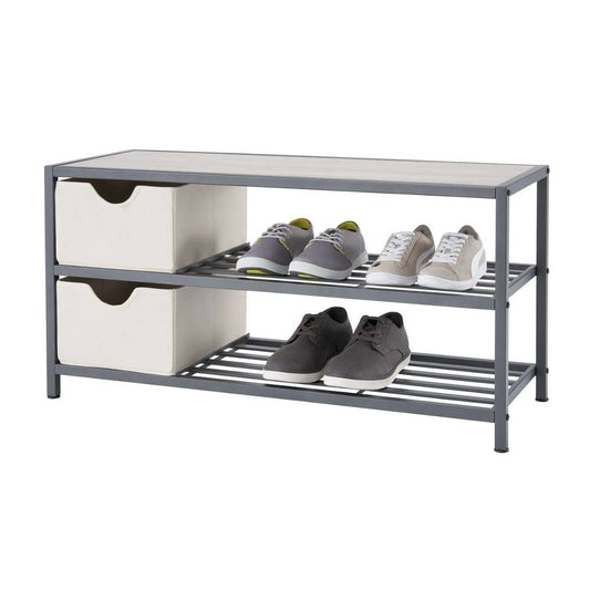 A three-tiered slate gray metal shoe bench with a light-colored top is shown against a white background. The middle and bottom shelves have horizontal slats and hold several pairs of shoes, while the top shelf also has two light-colored fabric storage baskets on the left side.