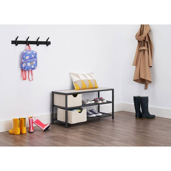 A wide shot shows a hallway with a three-tiered shoe bench with two light-colored fabric storage baskets on the middle shelf. The top shelf of the bench holds a patterned pillow and a few pairs of shoes, while more shoes are on the bottom metal rack.