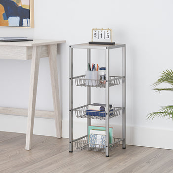 A light-colored, tall, rectangular shelf unit with three wire baskets is positioned next to a matching desk. The top shelf holds pens and a calendar, while the baskets contain various office supplies and documents.